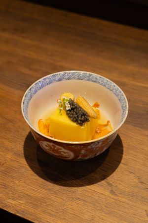 Yellow mango dessert garnished with caviar and microgreens served in a decorative blue and white bowl.