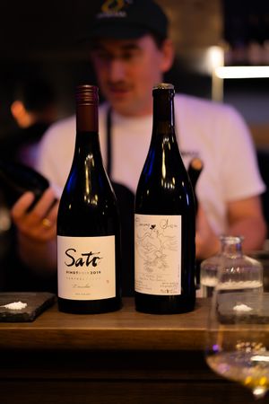 Collection of wine bottles displayed on a dark wooden bar counter in dim lighting.