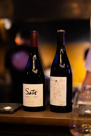 Wine bottles with handwritten labels arranged on a dark wooden surface in dim lighting.