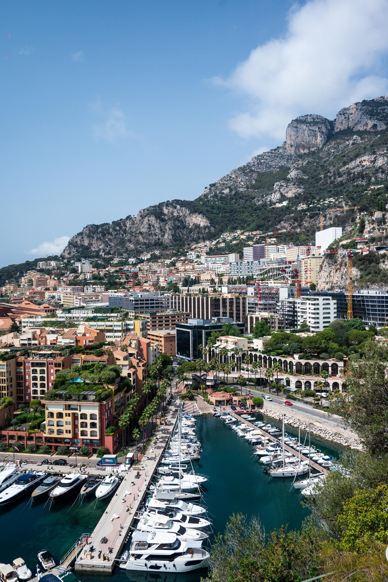 Panoramic view of Monaco's luxury marina with yachts docked against a backdrop of mountainous coastal architecture.