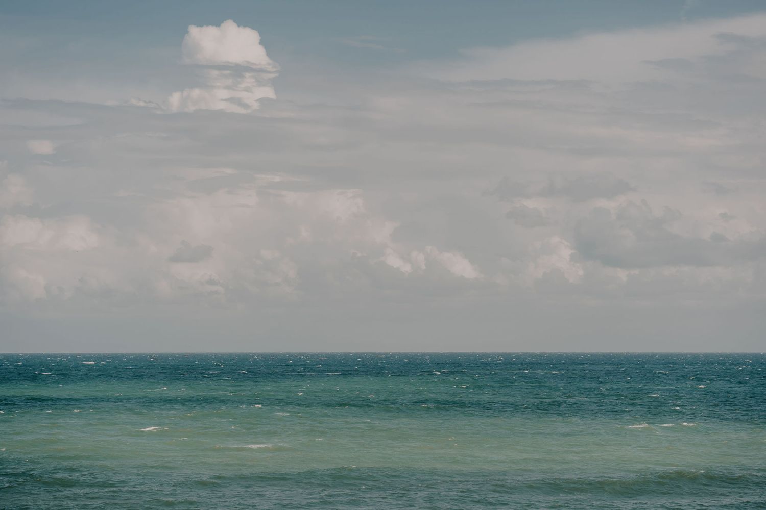 Serene seascape with fluffy clouds over turquoise waters stretching to the horizon.