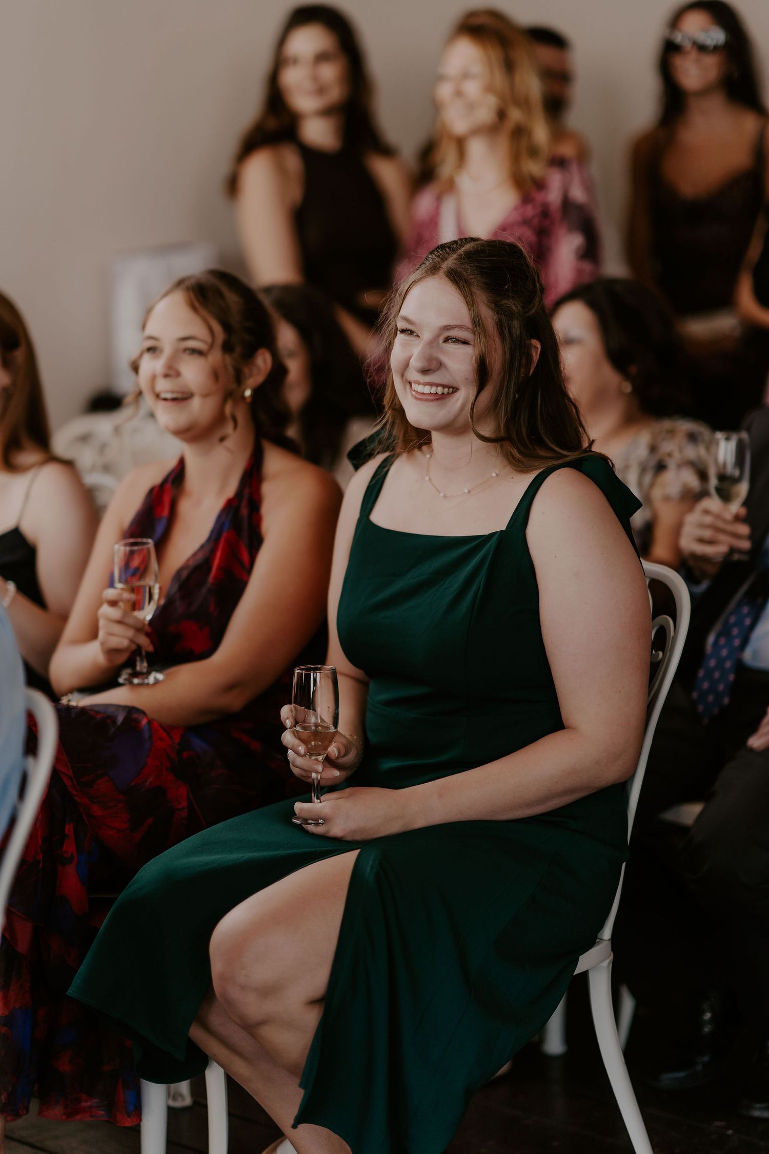 Wedding guests in dark dresses share joyful laughter while seated during a celebration.