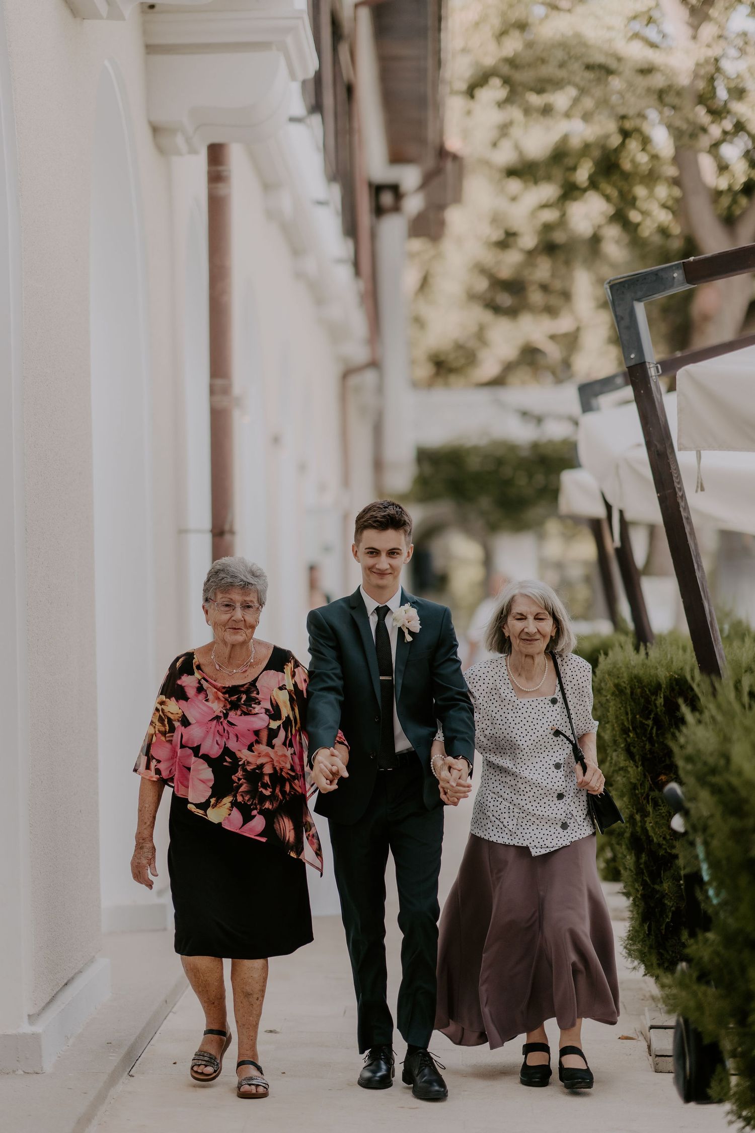 Wedding party members walk along an elegant white columned porch.