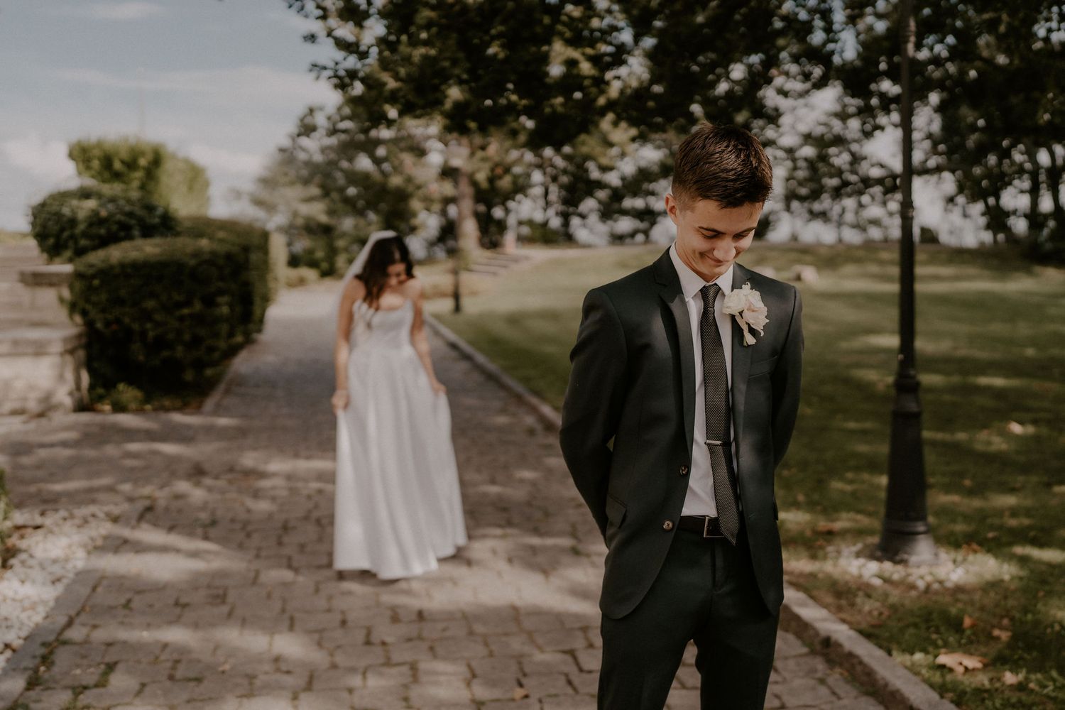 A couple shares their first look moment on a stone path with the bride approaching from behind.