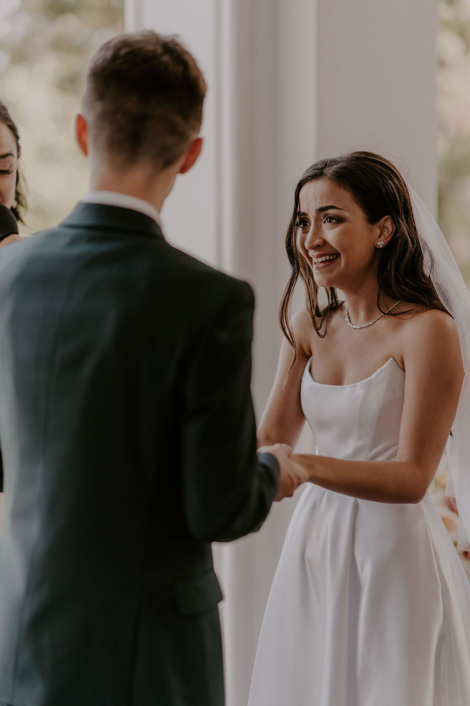 Joyful wedding ceremony moment captured during vow exchange under elegant white archways.