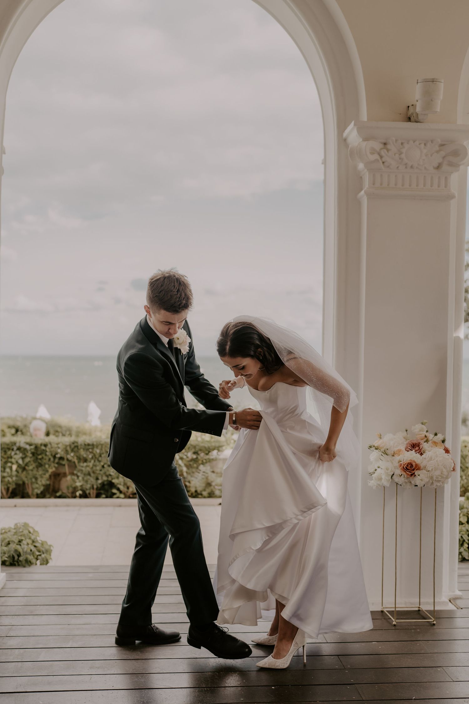 Newlyweds dance playfully under an arched doorway during their wedding photoshoot.