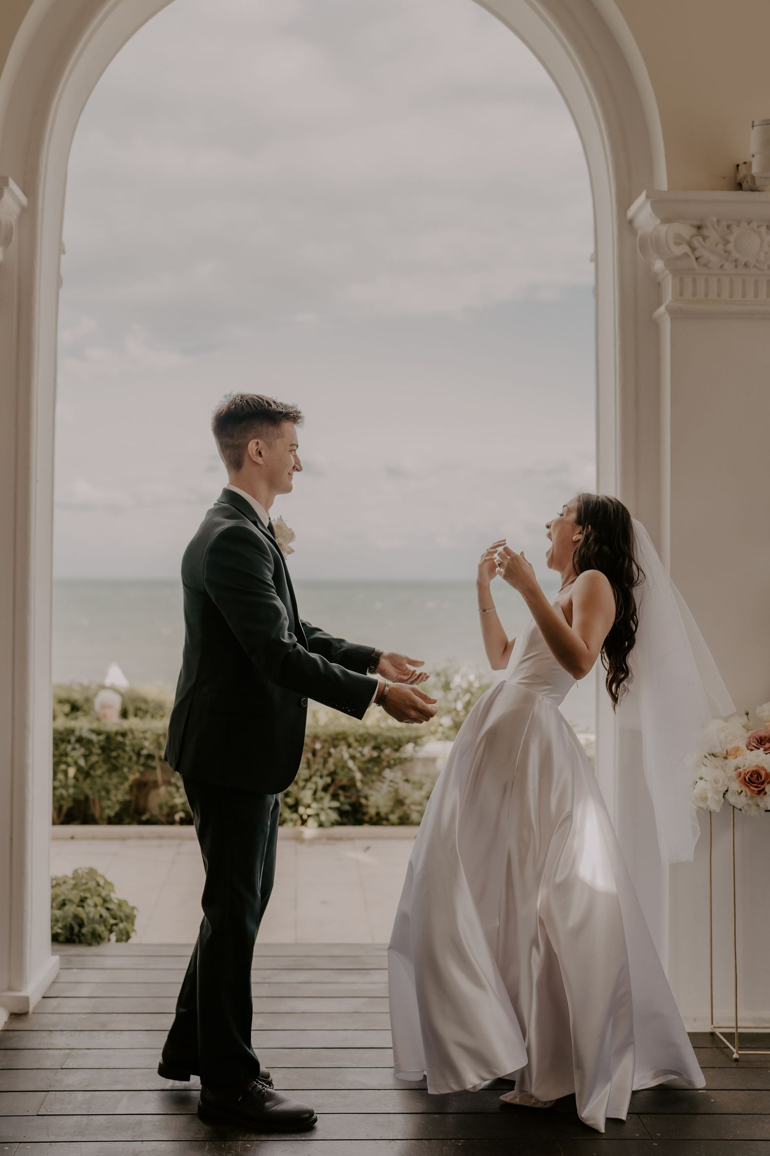A joyful wedding couple dances and laughs together on their special day under an elegant archway.