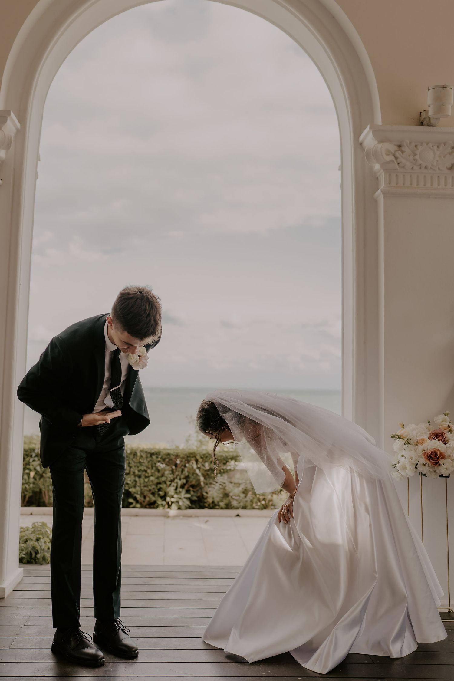 A couple shares a playful moment bowing to each other under an arched doorway.