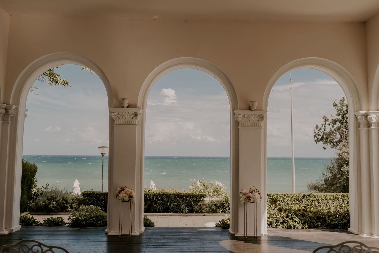 Elegant arched colonnade framing a stunning ocean view with white sand beach.