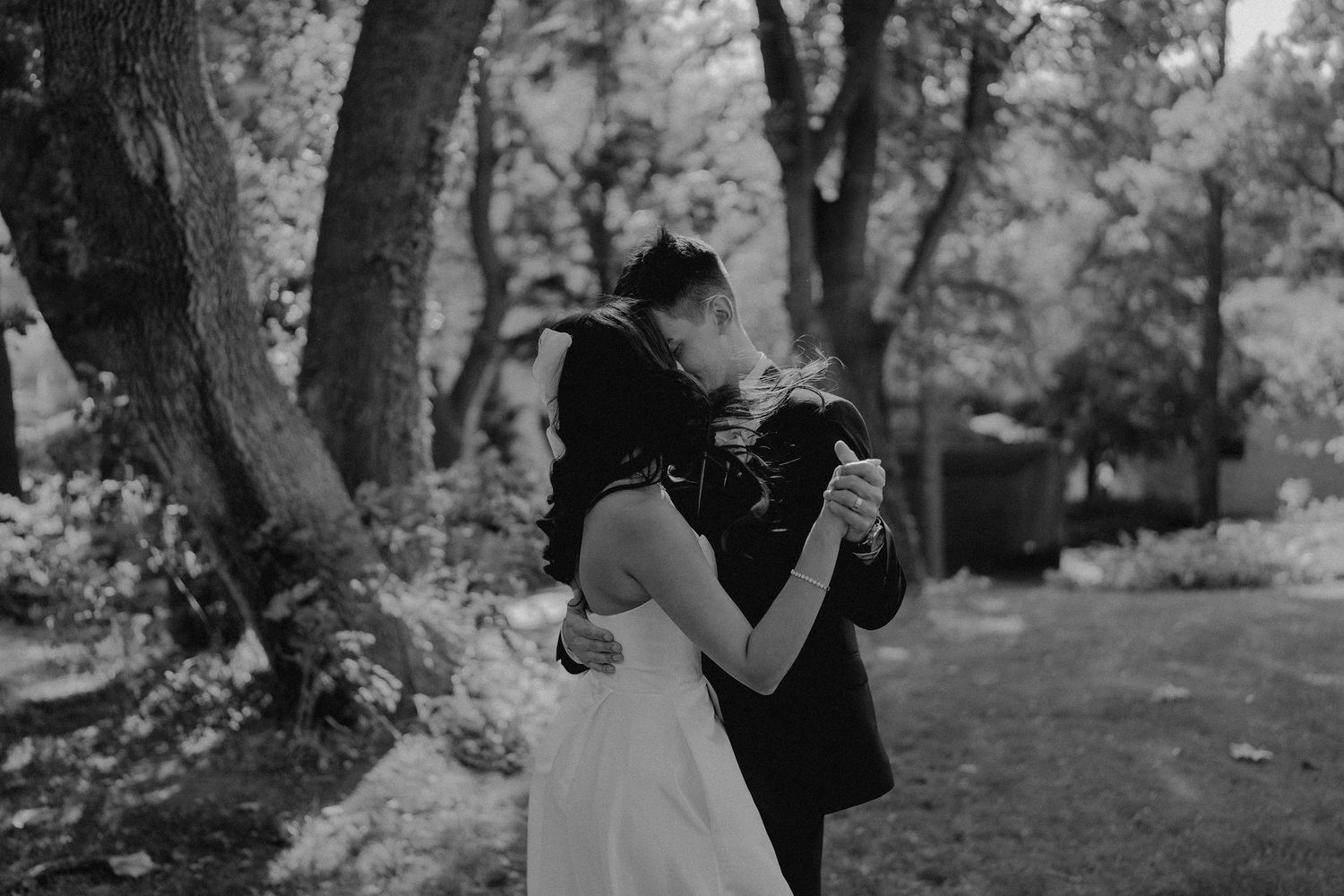 A black and white photo capturing an intimate dance between newlyweds outdoors.