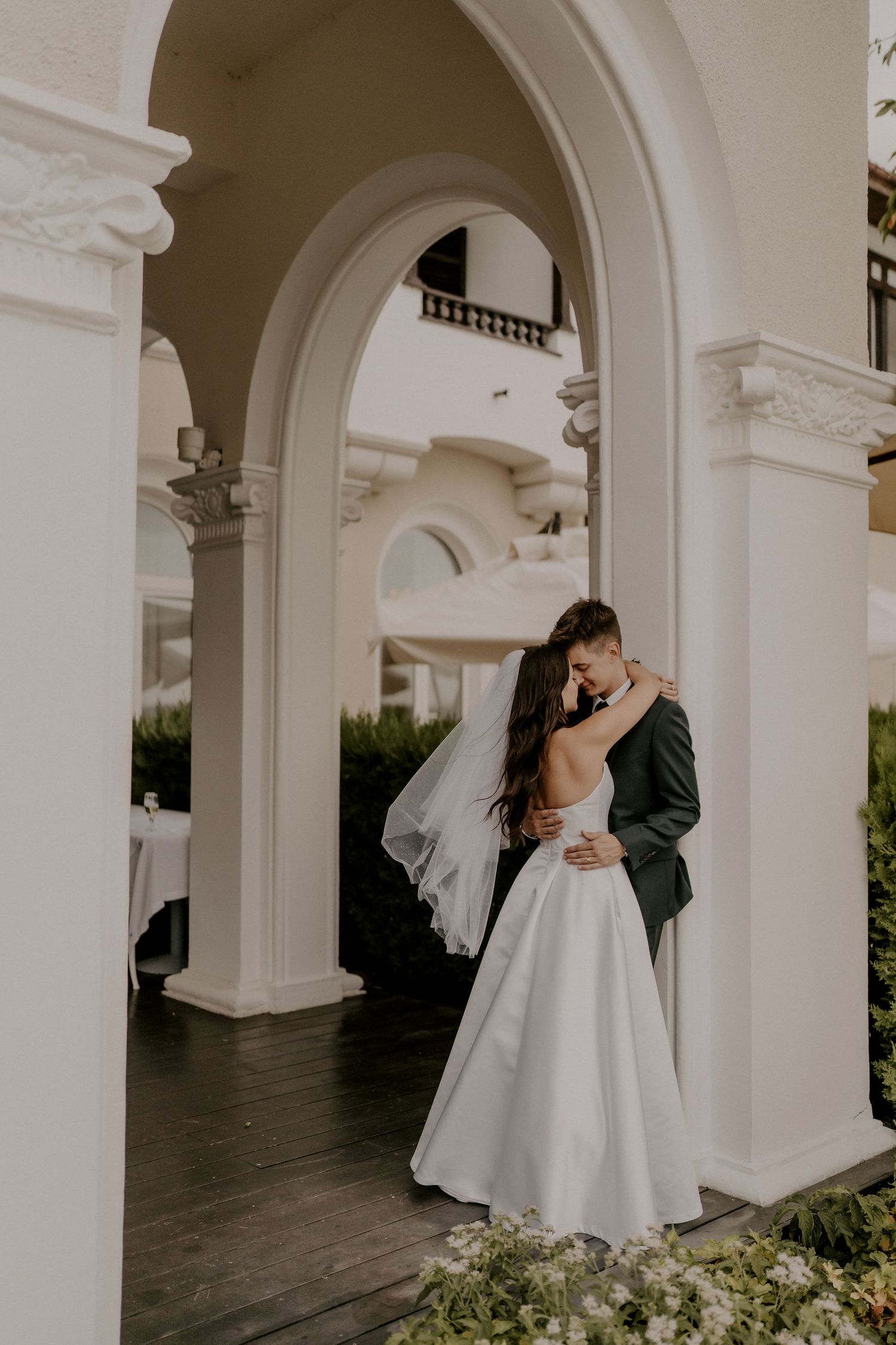 A romantic wedding couple shares intimate moments under elegant white archways.