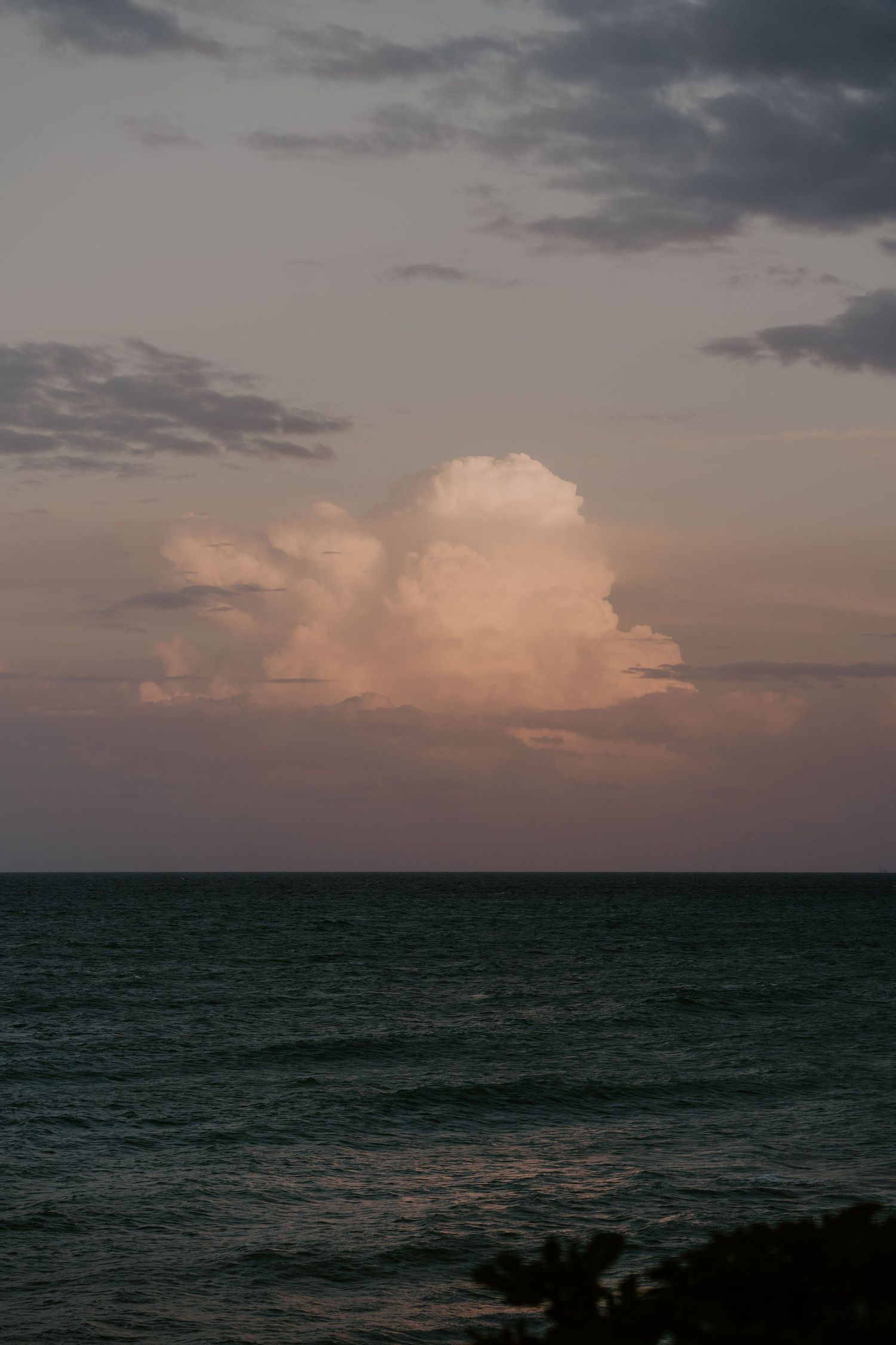 Dramatic sunset over the ocean with pink clouds and dark waters.