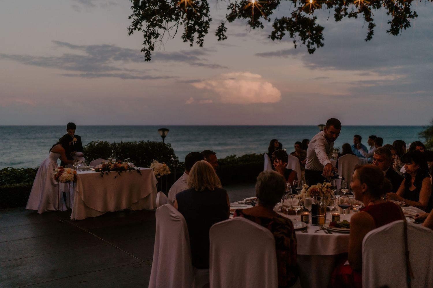 Outdoor wedding reception tables set up along the oceanfront at sunset.