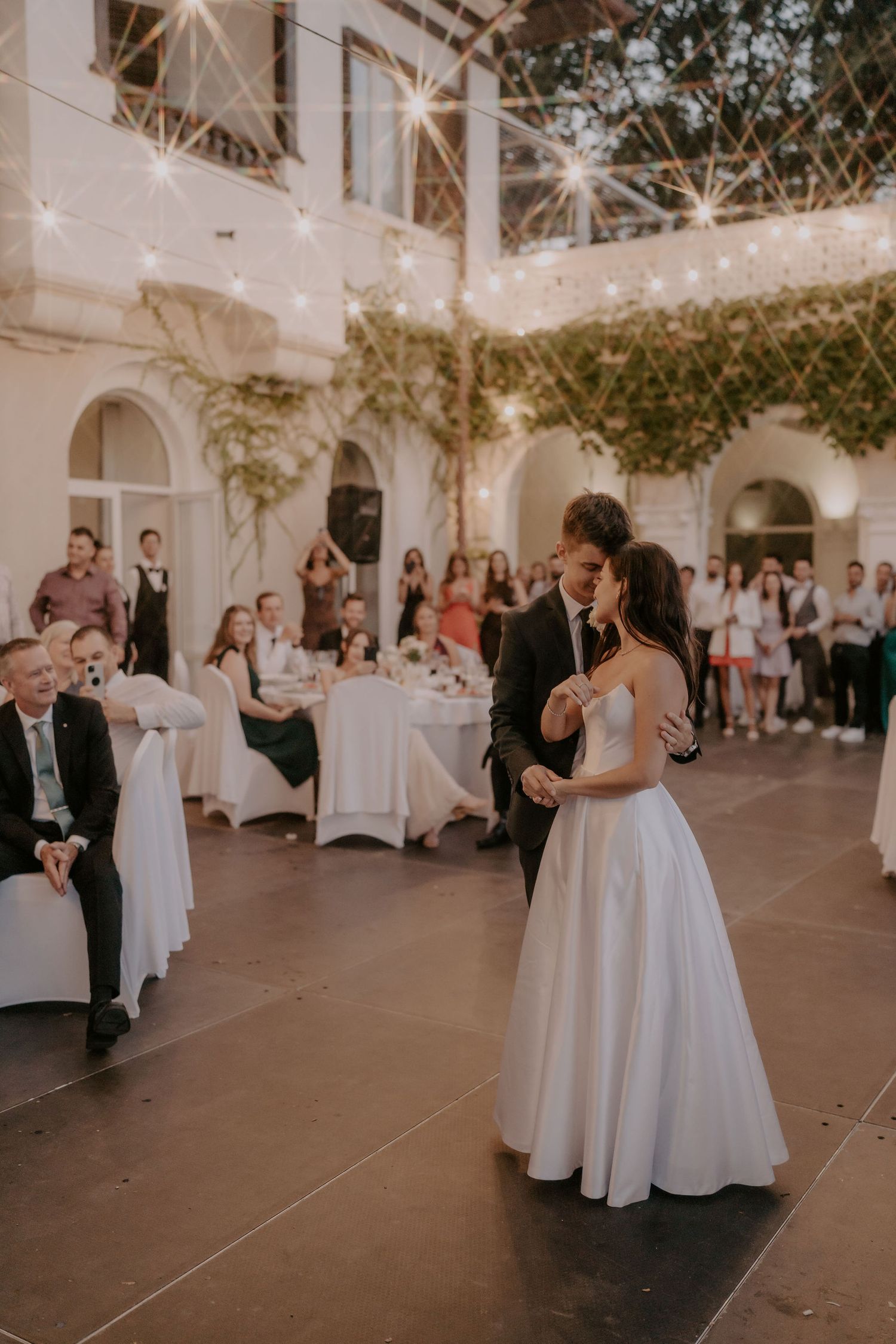 Couple shares an intimate dance moment in a beautiful courtyard reception with string lights overhead.