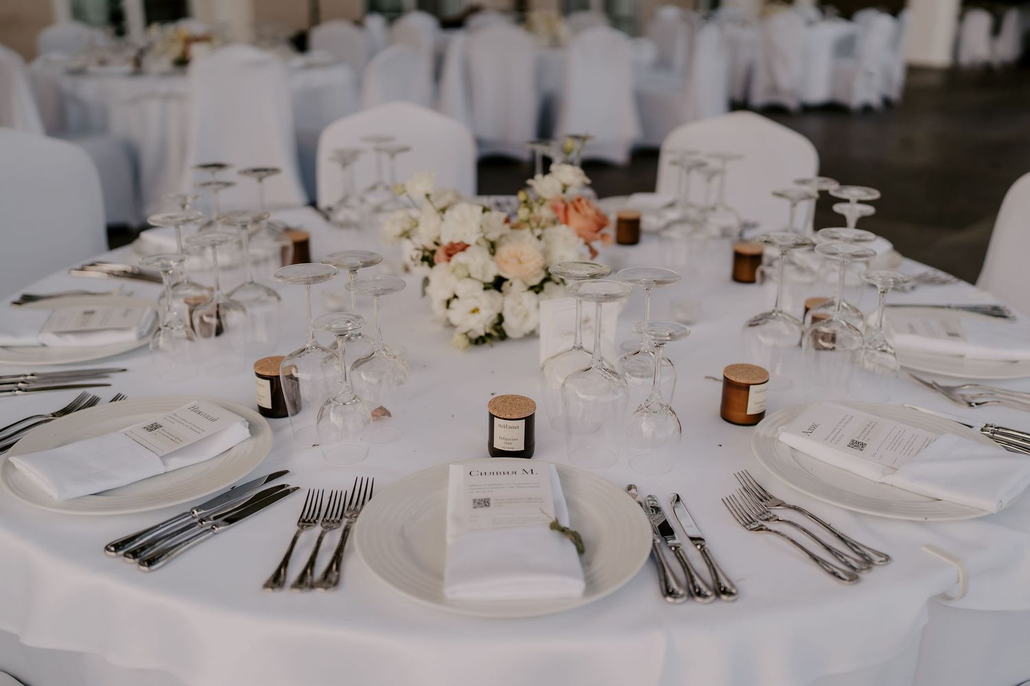 Close-up of elegant table settings with white linens and floral centerpieces at a formal event.