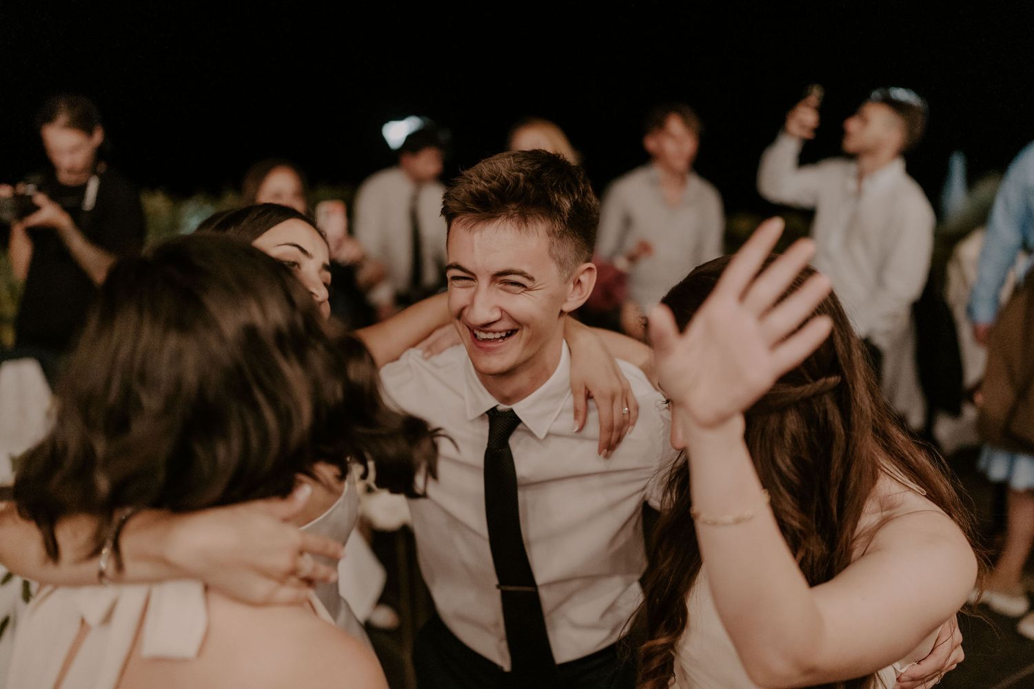 Wedding guests dance and embrace during a joyful reception celebration.