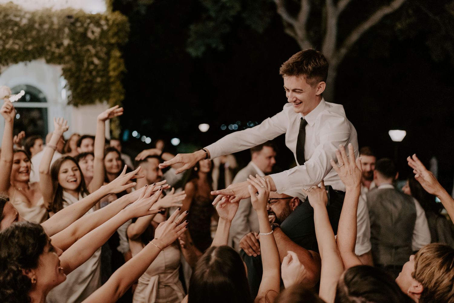 Wedding party members dance and celebrate with enthusiasm at an outdoor reception.