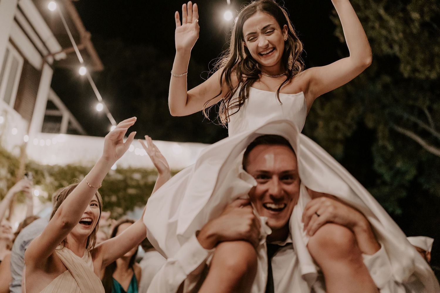 Wedding guests dance with raised arms during an energetic reception celebration.