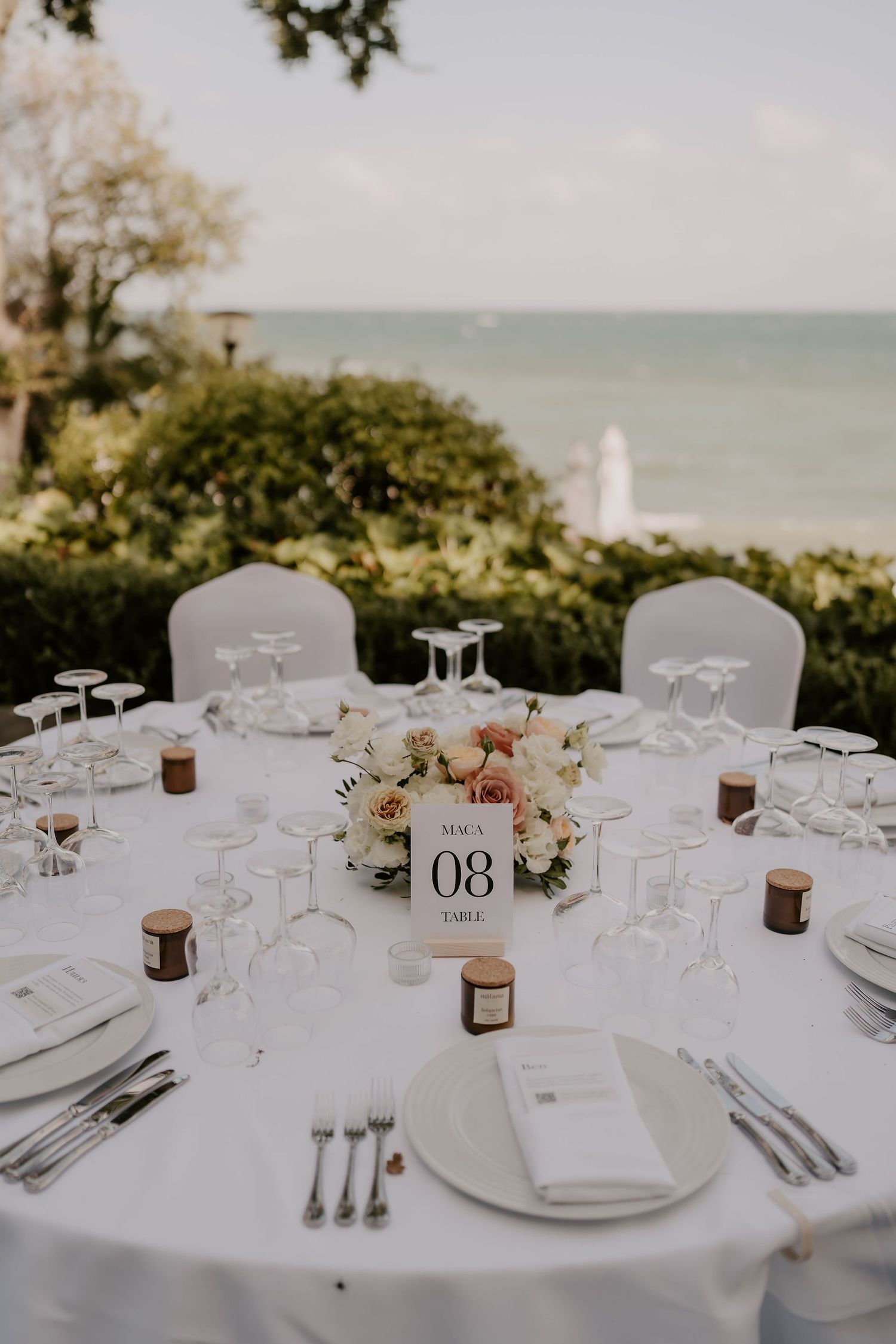 Wedding reception table overlooking the ocean with white linens and floral decorations.