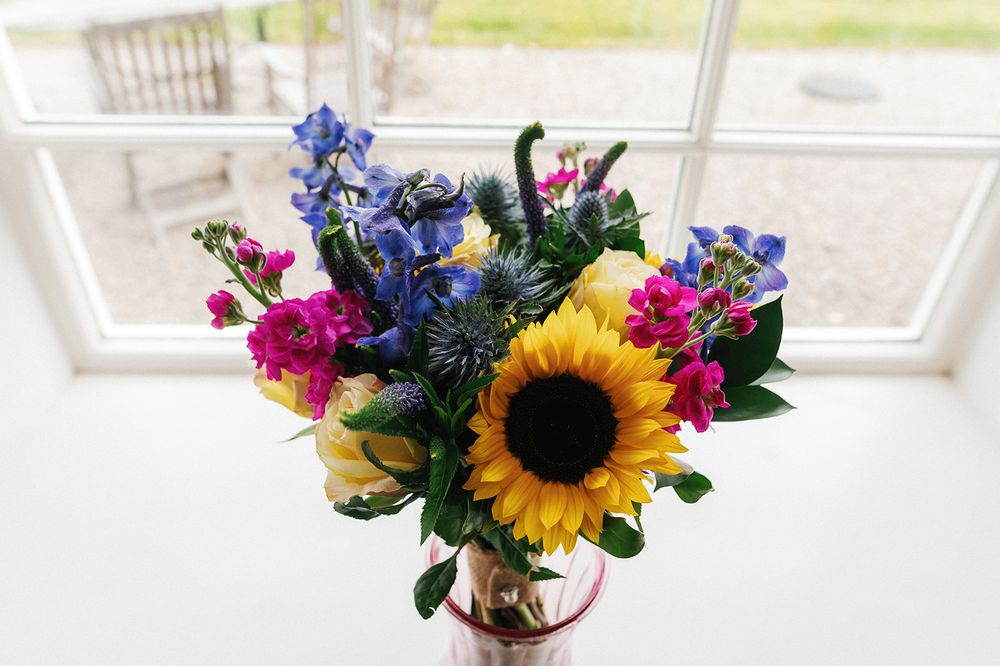 Vibrant wedding bouquet featuring sunflowers, blue delphiniums, and pink flowers in natural light.