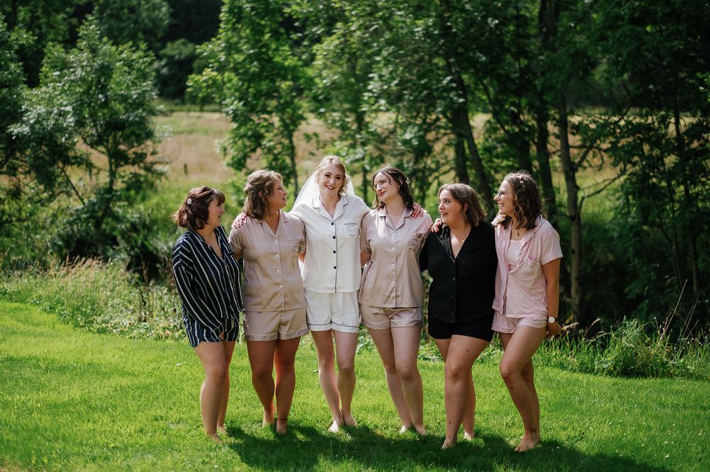 Group photo of wedding party members in light colored attire on a lush green lawn.