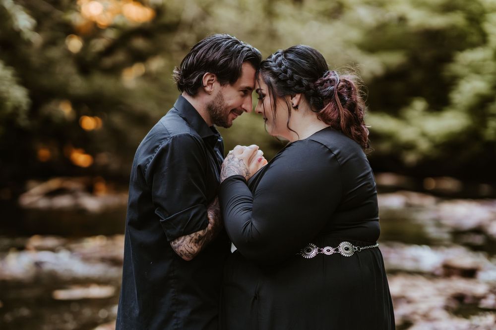 Intimate couple holding hands and touching foreheads near a peaceful forest creek.