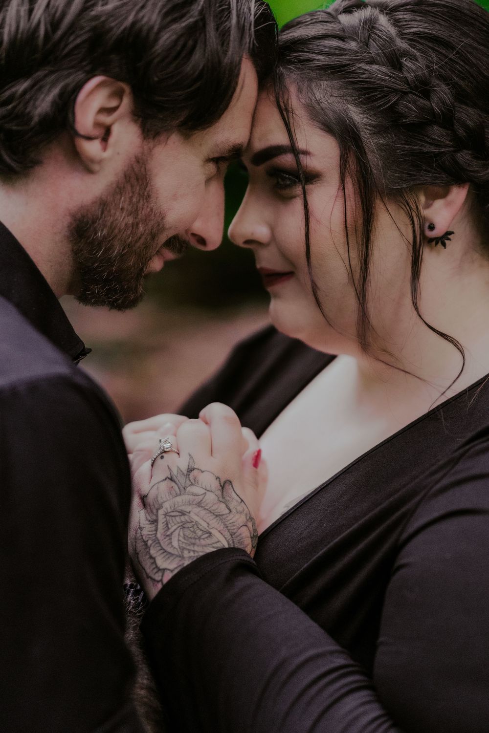 Close-up of couple touching foreheads, man with rose tattoo holding womans hands tenderly.