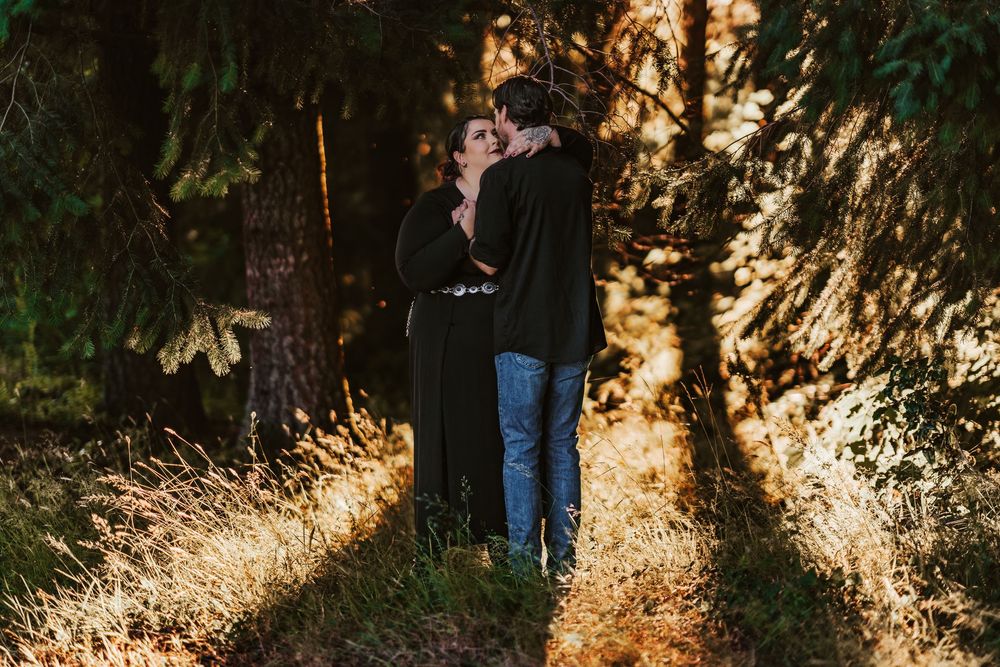 Couple sharing a romantic embrace on a sunlit forest trail among tall trees.