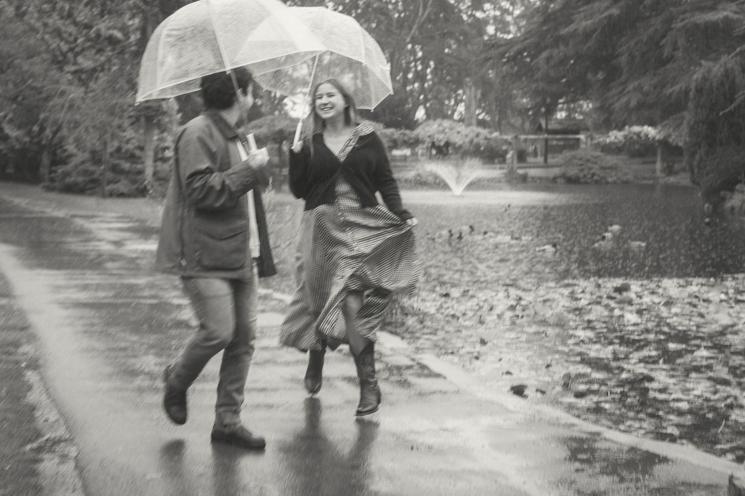People in a park playfully kicking and splashing through puddles of water on a rainy day.