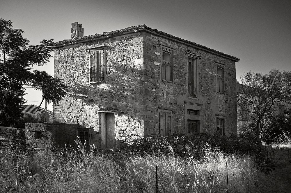 A panoramic view of an old abandoned stone building with multiple sections shown in black and white photography.