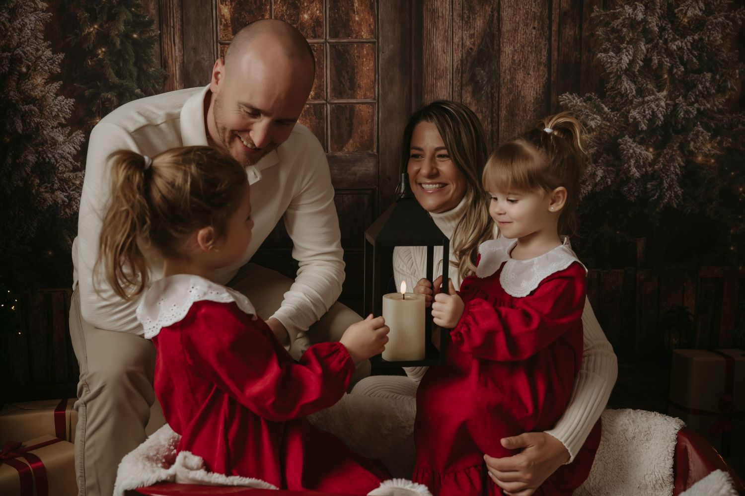 A family in coordinated red and white outfits shares a warm holiday moment together on a couch with rustic backdrop.