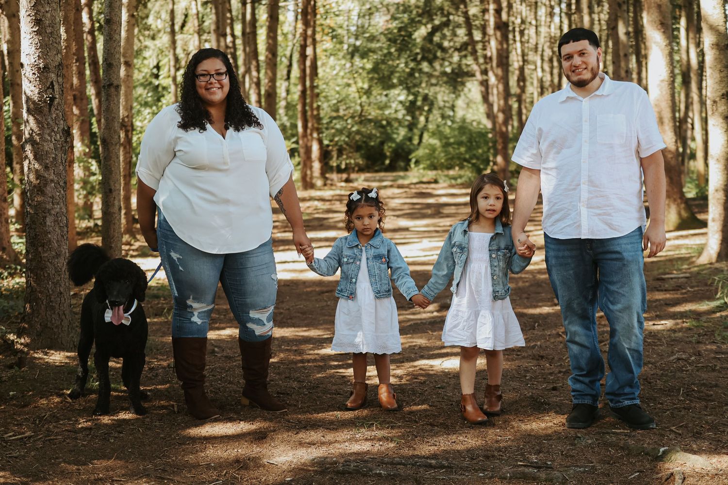 A group of people stand together in a wooded forest setting wearing coordinated white and denim outfits.