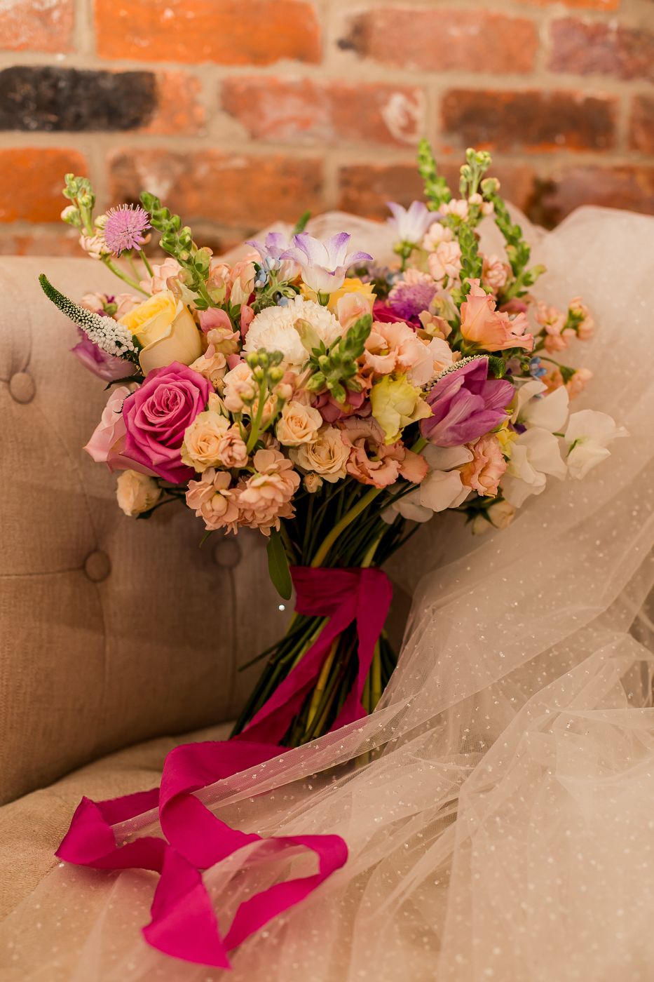 Wedding flower arrangements with pink ribbons displayed against exposed brick wall.