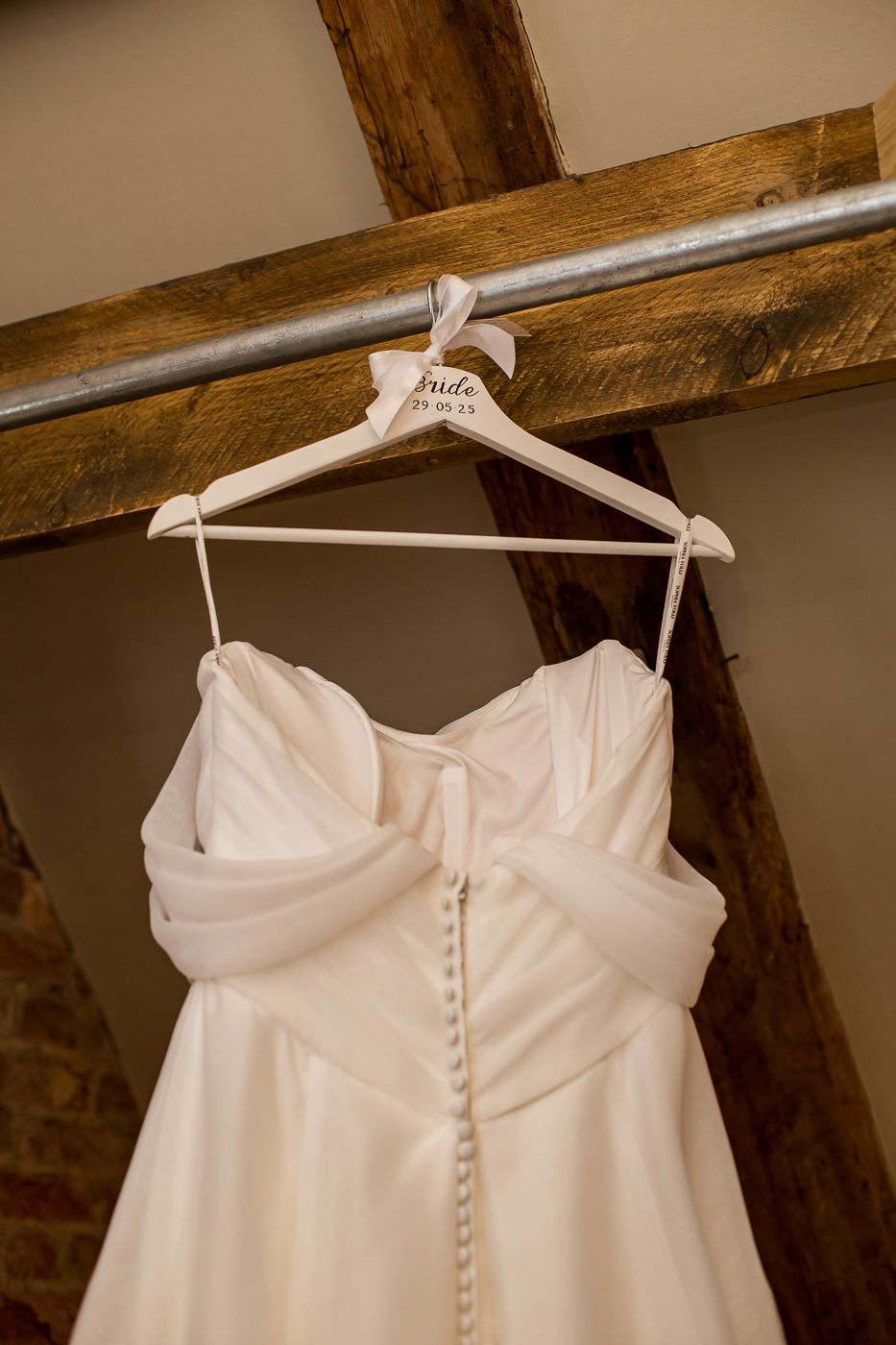 White wedding dress with button details hanging from wooden beams.