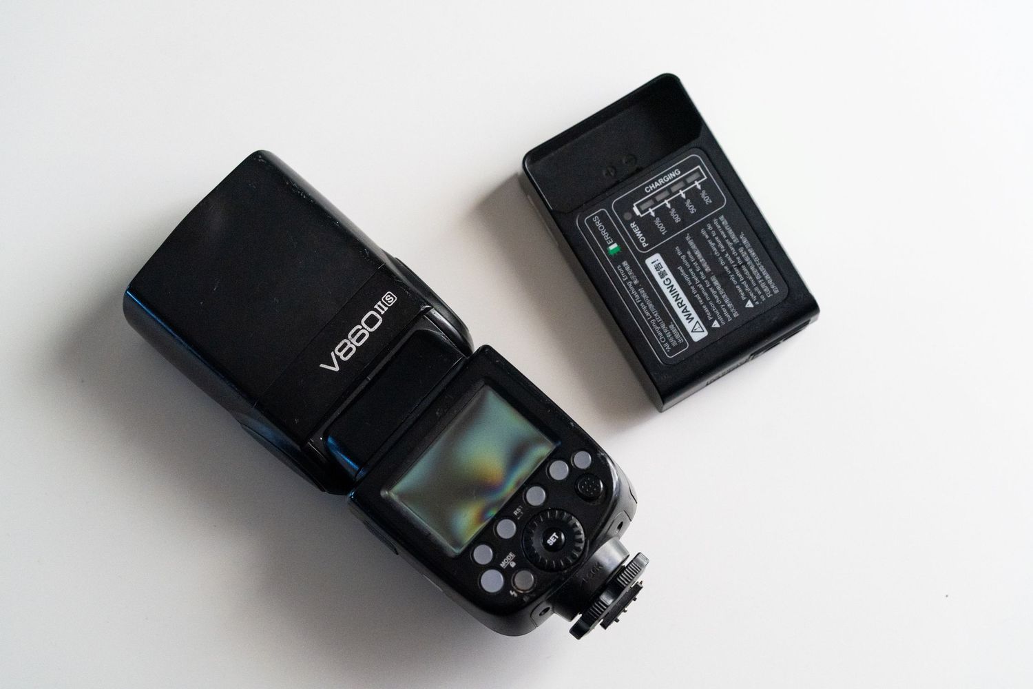 Black electronic camera flash unit with digital display and control buttons mounted on white surface.