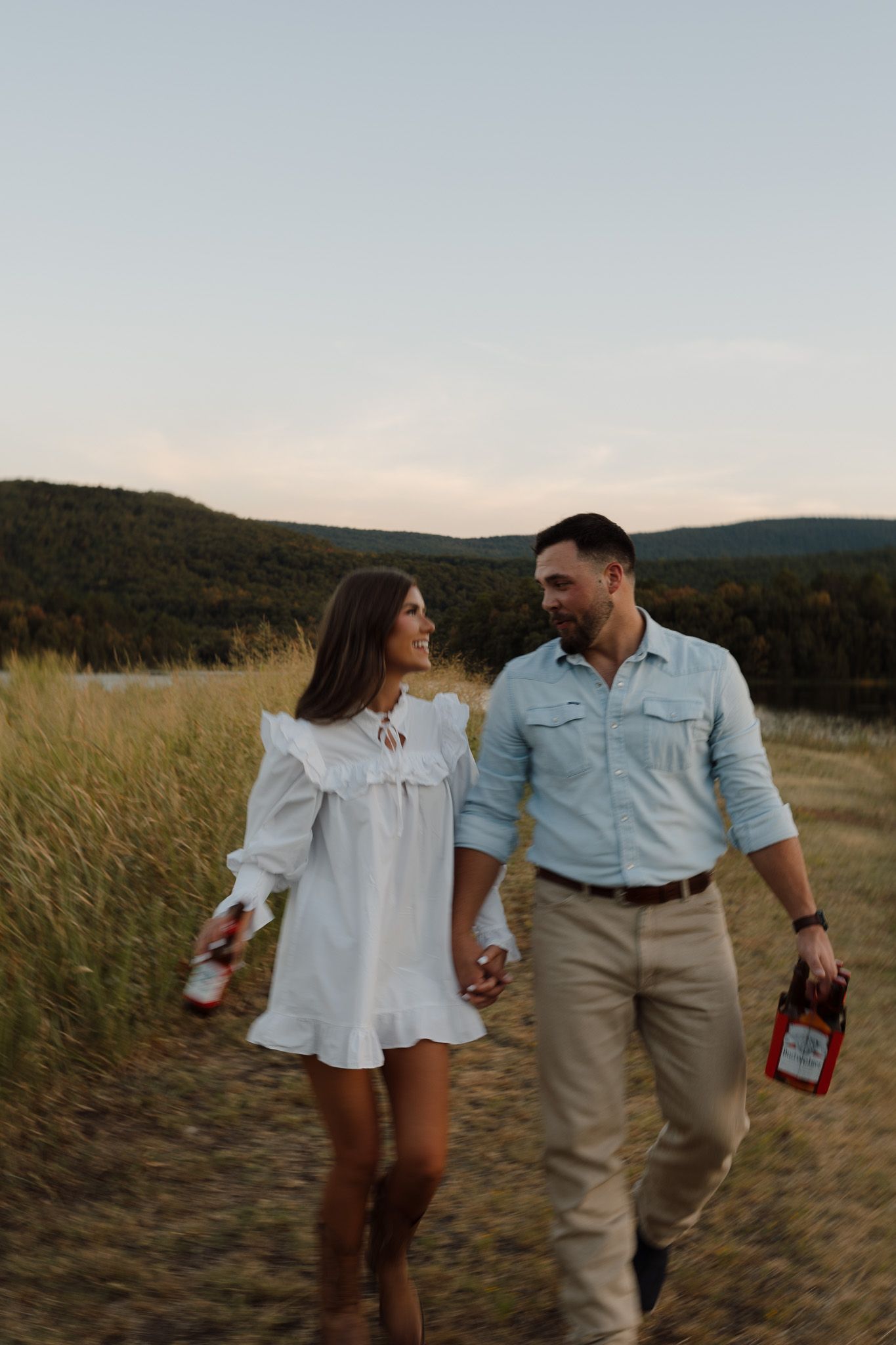 Loving couple embraces in golden sunset light in rustic field setting.