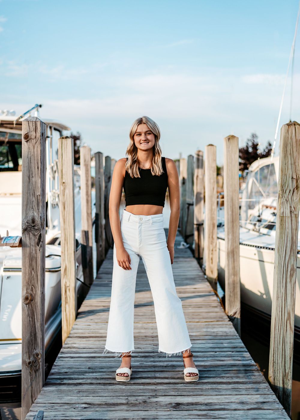 Stylish summer outfit featuring black crop top and white wide-leg pants on wooden marina dock with boats in background.