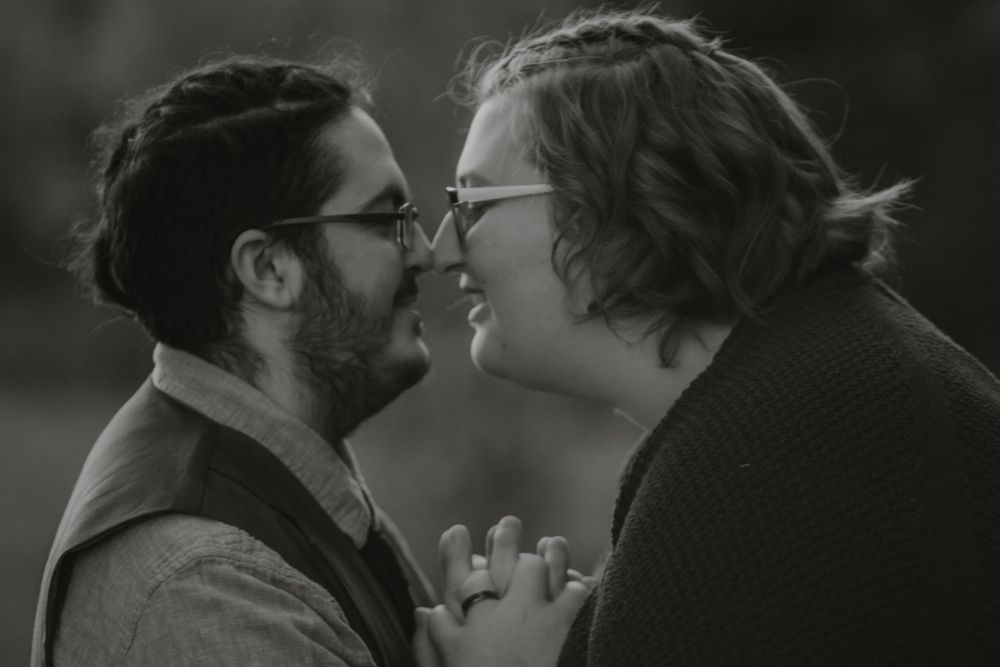 Black and white romantic close-up of engaged couple nearly kissing while holding hands outdoors.