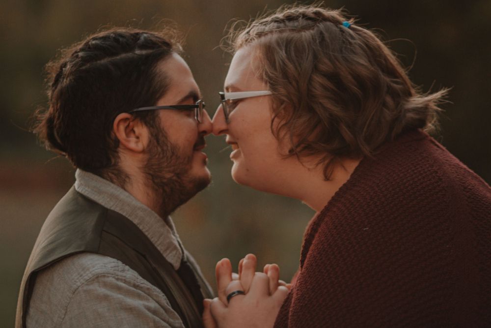 Close-up of smiling engaged couple nearly kissing while holding hands in romantic autumn setting.