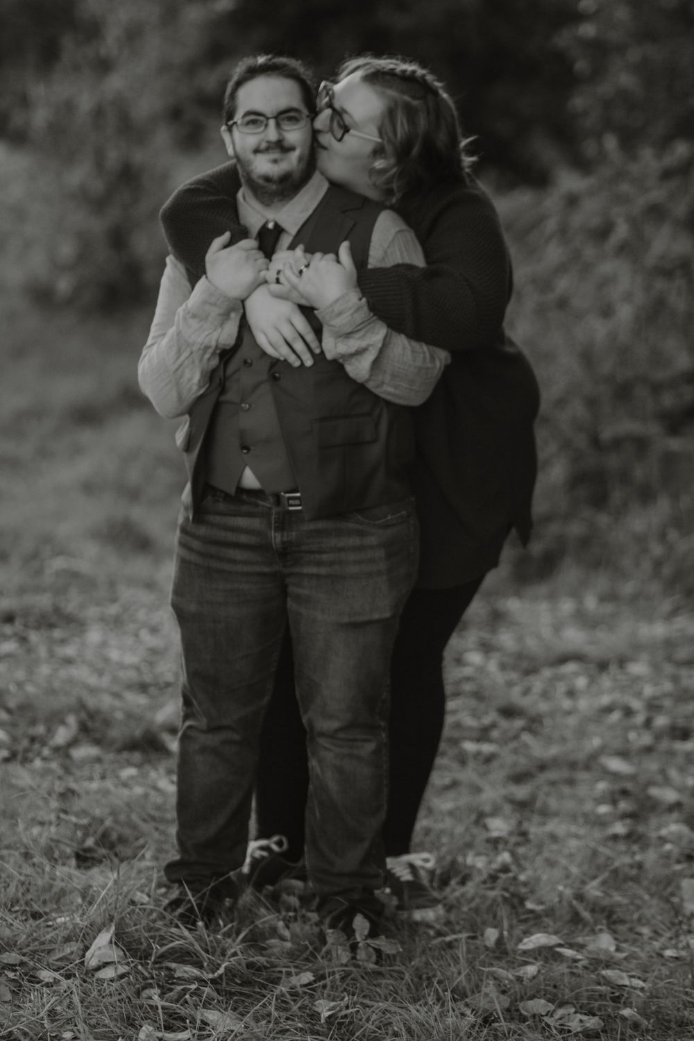 Black and white photo of woman hugging man from behind in autumn woodland engagement session.