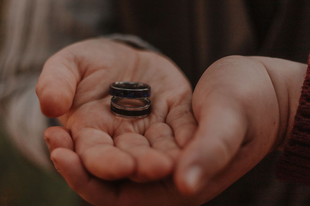 Two hands cupped together holding a dark wood and metal engagement ring in soft natural light.