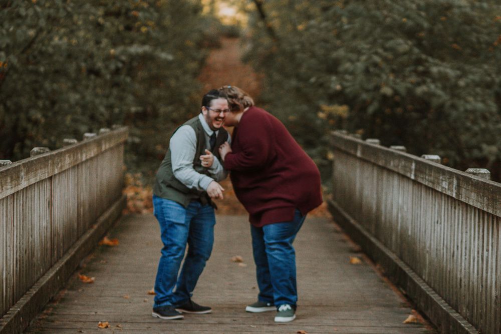 Joyful couple laughing together on wooden bridge during fall engagement photo session outdoors.