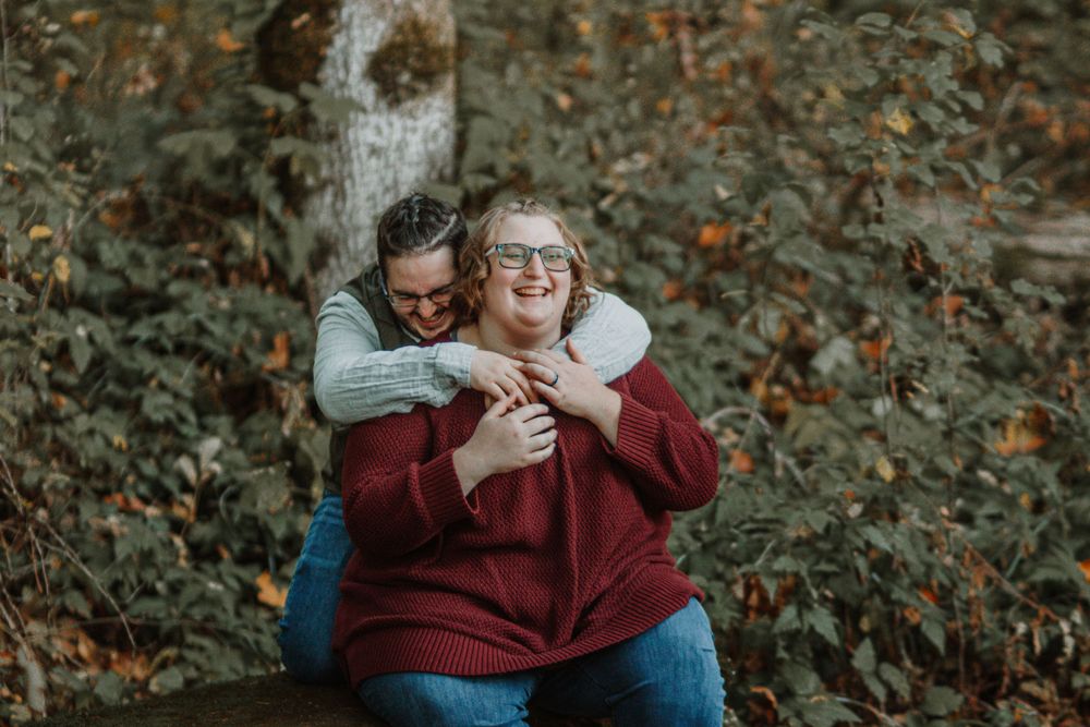 A couple shares a warm embrace sitting outdoors among colorful autumn foliage.