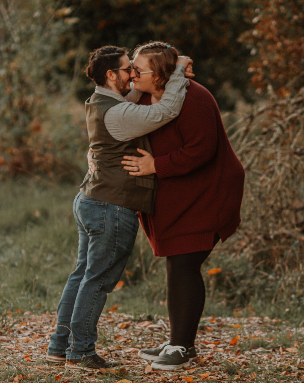 Couple embracing and laughing together in colorful fall foliage outdoor engagement photo session.