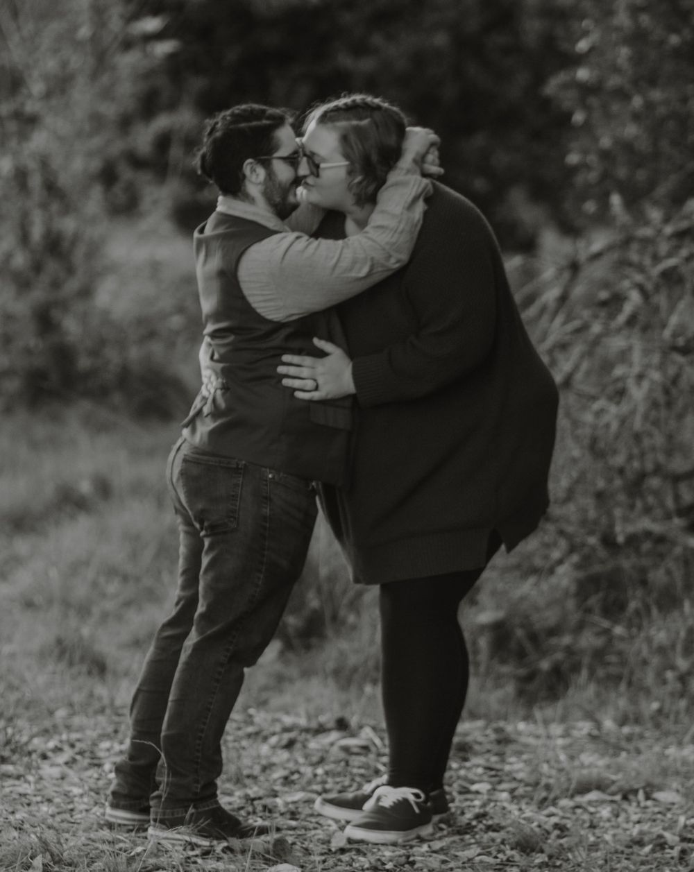 Black and white photo of a couple embracing and almost kissing in a natural outdoor setting.