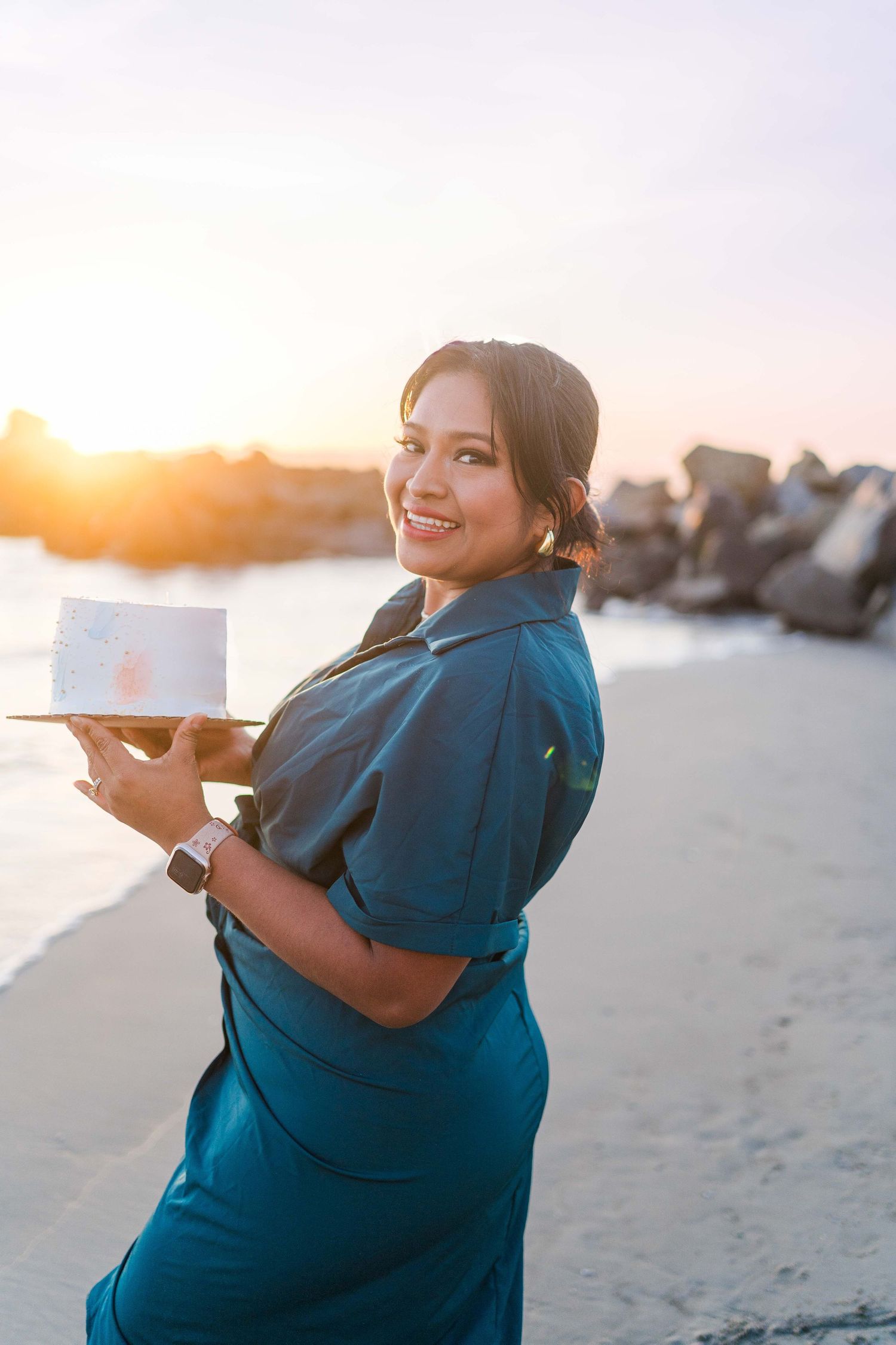 Person in a teal dress poses playfully on a sandy beach during sunset.
