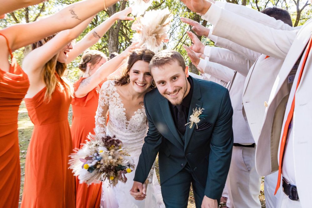 Wedding party celebrates with raised hands and joyful expressions in an outdoor setting.