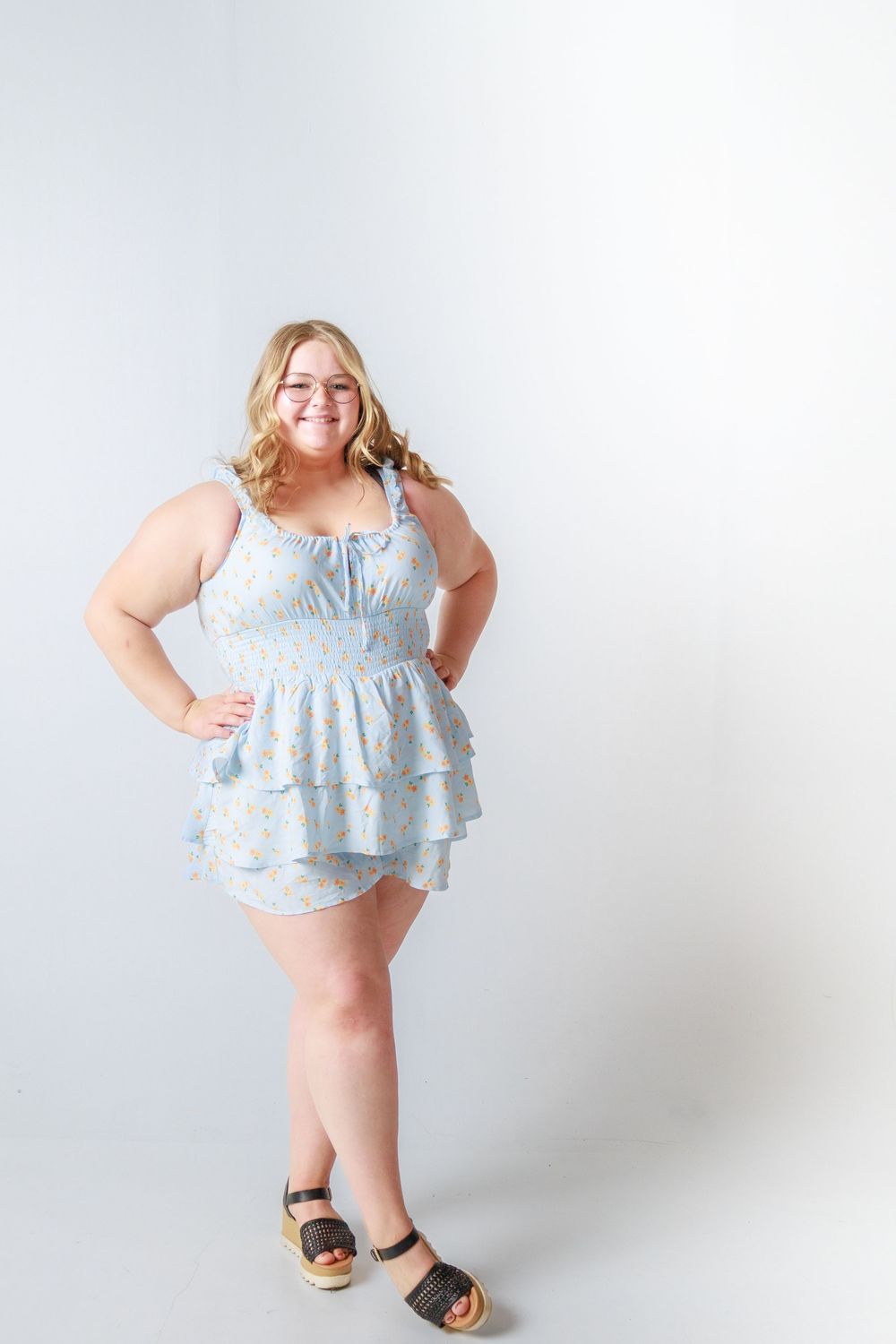 A person in a light blue ruffled sundress poses against a white background.
