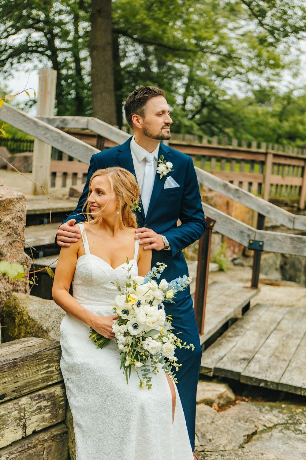 Wedding couple laughing together on rustic wooden boardwalk surrounded by trees.