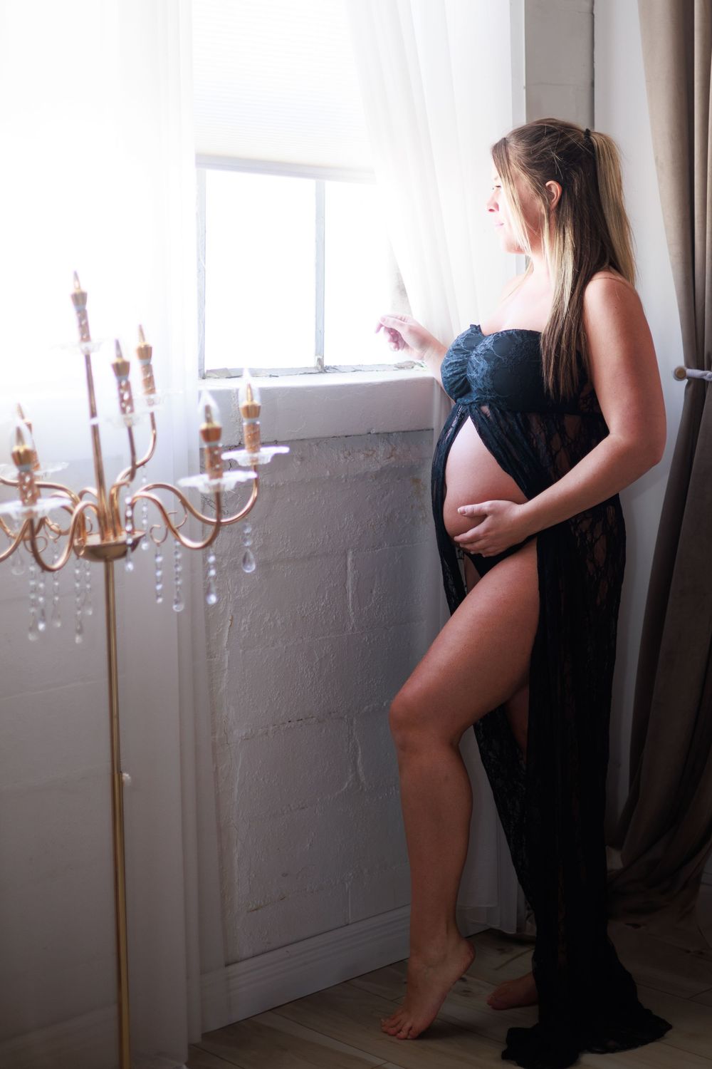 A maternity photo showing an elegant silhouette against window light with a vintage chandelier.